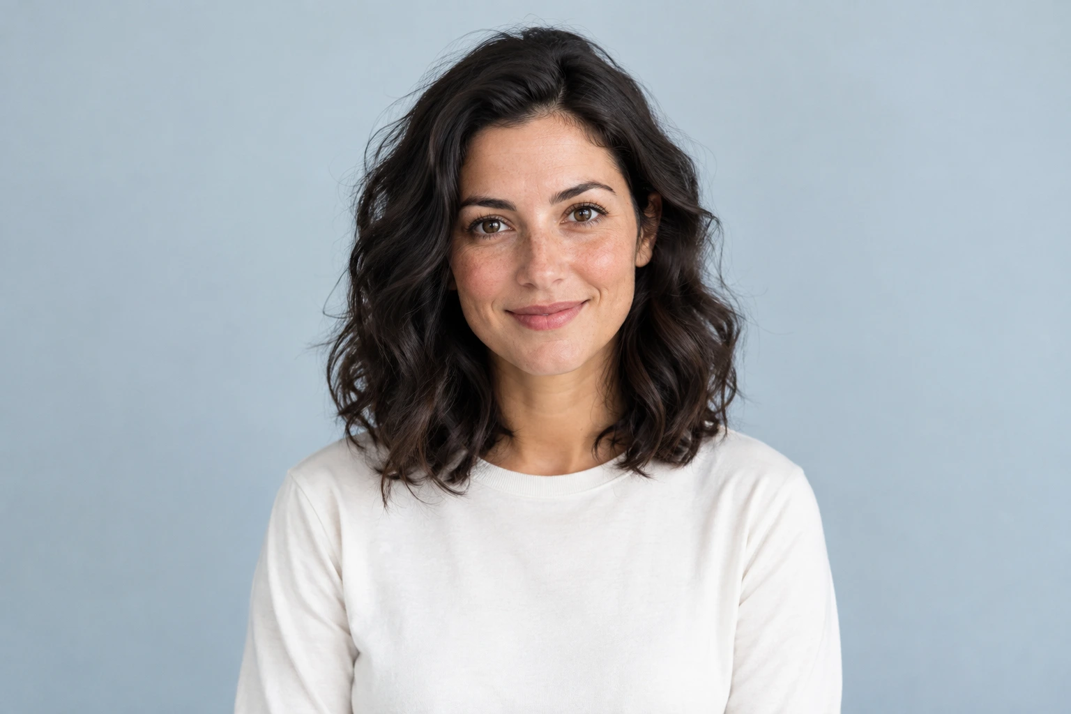 Contemporary studio portrait of an adult woman in an ivory shirt against a blue-gray backdrop.